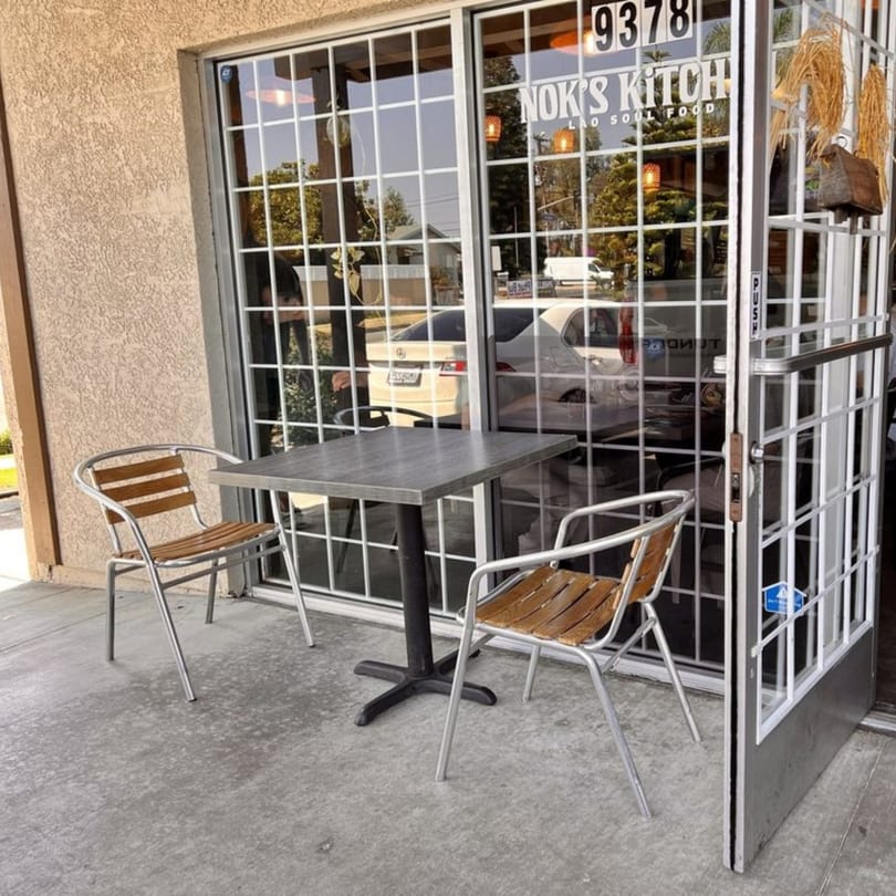 Outdoor seating area with a small table and two chairs in front of Nok's Kitchen.