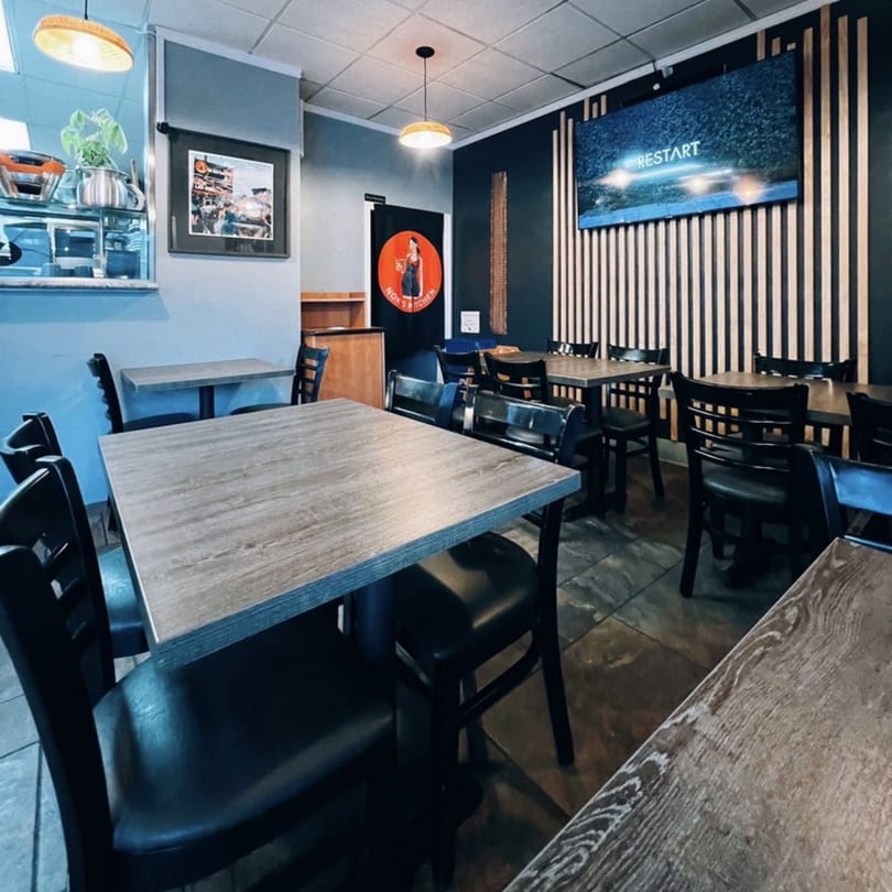 Interior of Nok's Kitchen, featuring dining tables, chairs, and a TV screen displaying "RESTART".